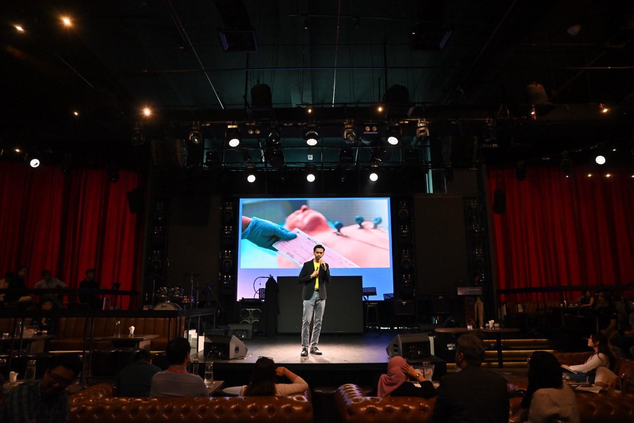 Alif on stage presenting ECG Sense to an audience, with an ECG being taken on the screen behind him